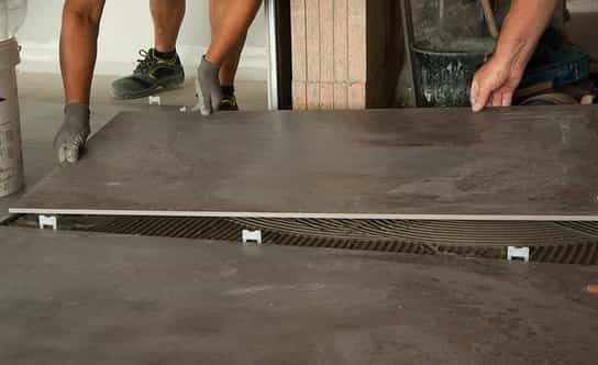 Carreleurs installent de gros carreaux de céramique dans l'entrée d'une société à Québec